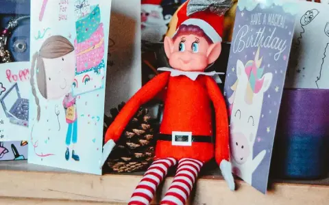 Un elfo di Natale, con il suo vestito rosso e calze a righe, è seduto tra biglietti d'auguri. La sua storia è legata alla magia delle feste e dei compleanni.