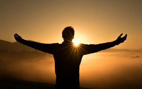 Silhouette di una persona con le braccia aperte al tramonto, immersa nella nebbia dorata. Un momento di pace e buonanotte con gratitudine.
