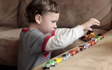 Bambino gioca con macchinine, creando una fila colorata. Le sue mani si muovono con un ritmo ipnotico, un esempio di stimming mani.
