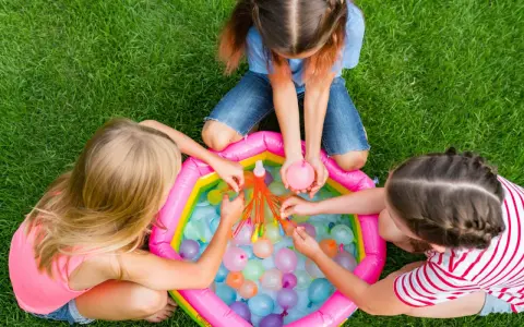 Bambini di 6 anni si divertono con giochi d'acqua in giardino, perfetti per un compleanno estivo.