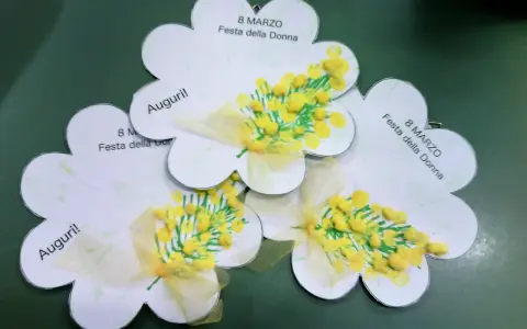 Lavoretto festa della donna infanzia: tre fiori di carta con mimose dipinte e fiocchi gialli. Scritte "Auguri!" e "8 Marzo Festa della Donna".