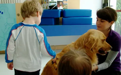 Un bambino interagisce con un cane durante una sessione di pet therapy. La donna sorride mentre il cane è accarezzato.