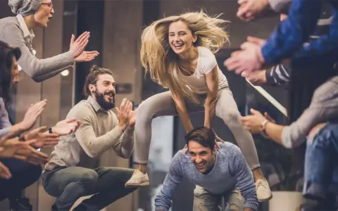 Un gruppo di amici si diverte con giochi da fare in gruppo seduti senza niente, una donna salta su un uomo mentre gli altri applaudono.
