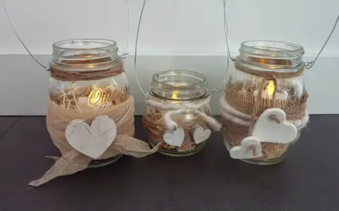 Tre vasetti lanterne fai da te decorati con cuori e spago, con candele accese all'interno per un'atmosfera calda.