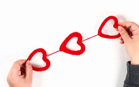 Mani che creano cuori rossi di lana, perfetti per lavoretti per San Valentino.