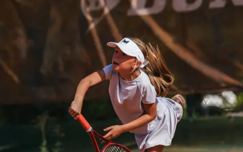 Bambina concentrata durante un servizio di tennis, con la racchetta pronta a colpire la palla.