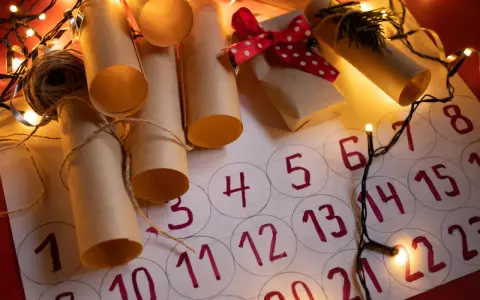 Un **calendario avvento fai da te cartoncino** con rotoli di carta marrone legati con spago, luci natalizie e un piccolo pacchetto regalo.