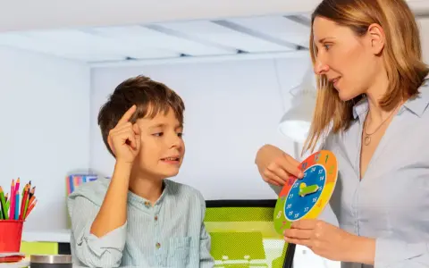 Bambino concentrato durante una sessione di terapia occupazionale, impara a leggere l'ora con un colorato orologio didattico.