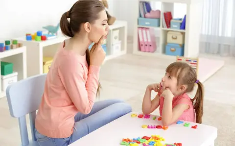 Logopedista e bambina fanno esercizi di logopedia con lettere colorate sul tavolo.