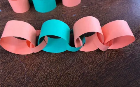 Una catena di carta colorata, con anelli arancioni e verdi intrecciati, pronta per decorare.