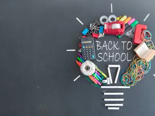 Un'idea luminosa per un buon inizio di anno scolastico: calcolatrice, penne, elastici e altri materiali scolastici formano una lampadina su lavagna.