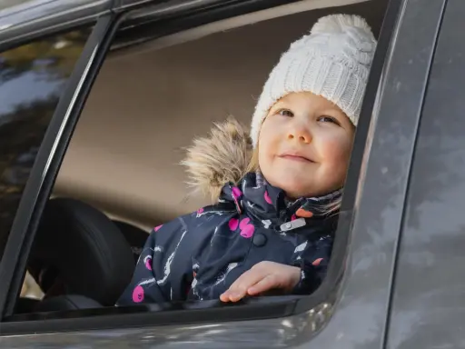Bambina con cappellino bianco guarda fuori dal finestrino, pronta per i giochi da fare in macchina bambini.