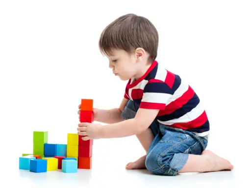 Bambino costruisce torre con blocchi colorati, esercitando la motricità fine. Obiettivi per lo sviluppo cognitivo e manuale.