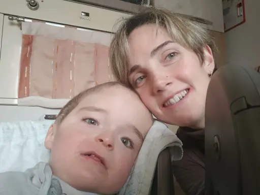 Un bambino con sindrome di down lieve e sua madre sorridono. La sua espressione dolce e i suoi occhi chiari sono un segno di amore.