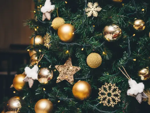 Un albero di Natale addobbato con palline dorate, fiocchi di neve scintillanti e stelle di stoffa. Le luci gialle creano un'atmosfera magica, un vero simbolo albero di natale.