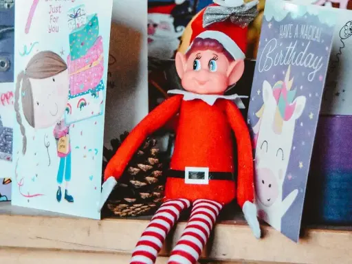 Un elfo di Natale, con il suo vestito rosso e calze a righe, è seduto tra biglietti d'auguri. La sua storia è legata alla magia delle feste e dei compleanni.