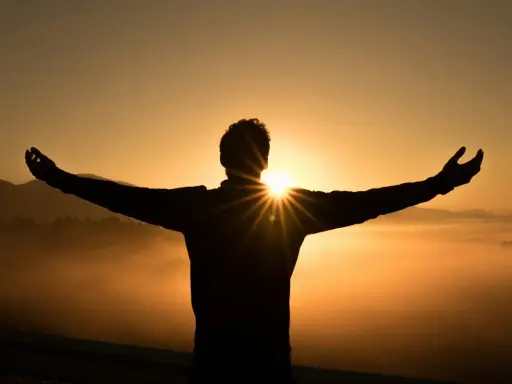 Silhouette di una persona con le braccia aperte al tramonto, immersa nella nebbia dorata. Un momento di pace e buonanotte con gratitudine.