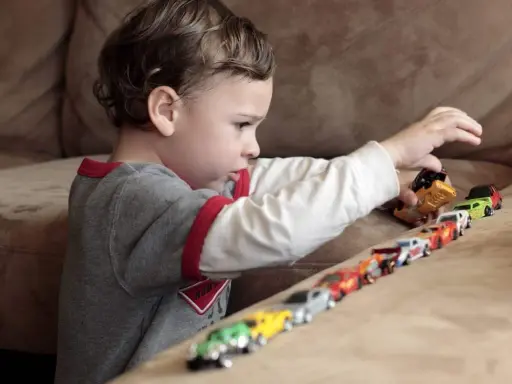 Bambino gioca con macchinine, creando una fila colorata. Le sue mani si muovono con un ritmo ipnotico, un esempio di stimming mani.
