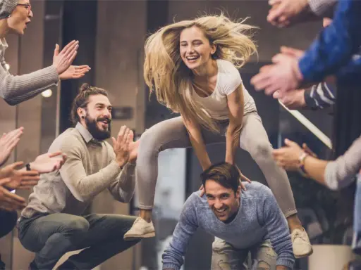Un gruppo di amici si diverte con giochi da fare in gruppo seduti senza niente, una donna salta su un uomo mentre gli altri applaudono.