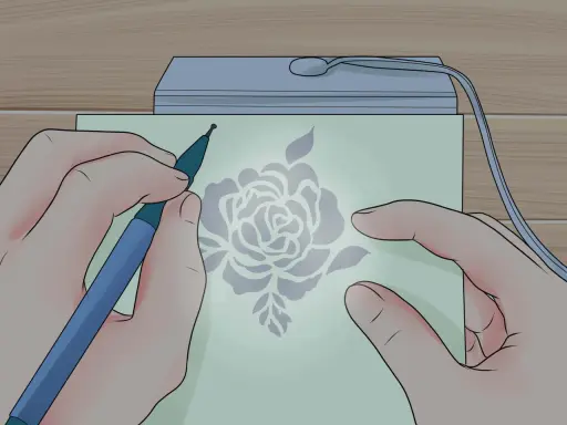 Mani che creano un disegno floreale con uno strumento su carta illuminata, un'arte di embossing su carta.