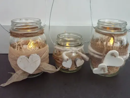 Tre vasetti lanterne fai da te decorati con cuori e spago, con candele accese all'interno per un'atmosfera calda.