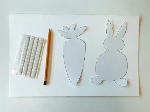 Sagoma di coniglietto e carota, matita e adesivi per creare decorazioni pasquali.