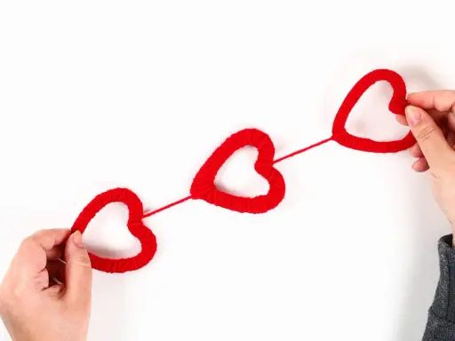 Mani che creano cuori rossi di lana, perfetti per lavoretti per San Valentino.