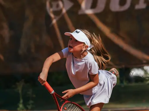 Bambina concentrata durante un servizio di tennis, con la racchetta pronta a colpire la palla.
