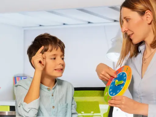 Bambino concentrato durante una sessione di terapia occupazionale, impara a leggere l'ora con un colorato orologio didattico.