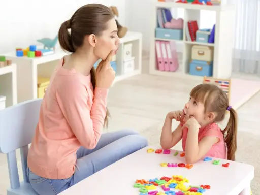 Logopedista e bambina fanno esercizi di logopedia con lettere colorate sul tavolo.