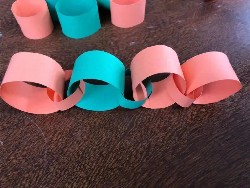 Una catena di carta colorata, con anelli arancioni e verdi intrecciati, pronta per decorare.