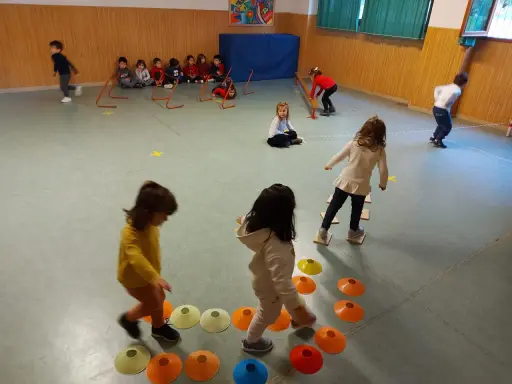Bambini si divertono con giochi psicomotricità 3 anni: corrono, saltano ostacoli e camminano su coni colorati in palestra.