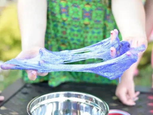 Mani che creano slime glitterato viola, un divertente esperimento su come si fa lo slime.