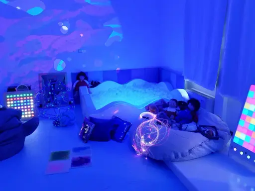 Stanza sensoriale autismo con piscina di palline, luci soffuse, pupazzi e pannelli interattivi per stimolare i sensi.