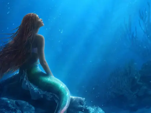 La sirenetta storia breve: una giovane sirena dai capelli rossi guarda verso l'alto, sognando il mondo di sopra, seduta su una roccia sottomarina.