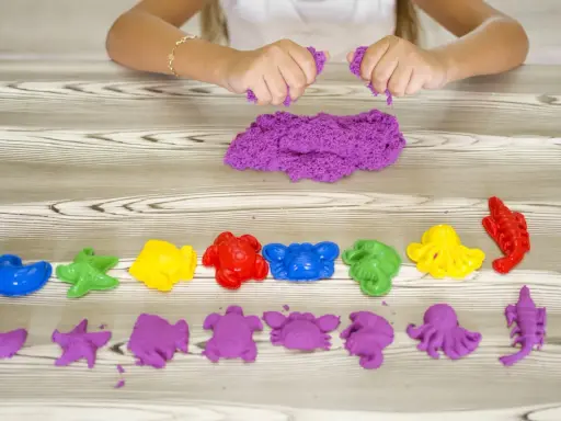 Bambina gioca con sabbia cinetica da che età? Formine marine colorate e viola, un divertimento sensoriale per tutti.