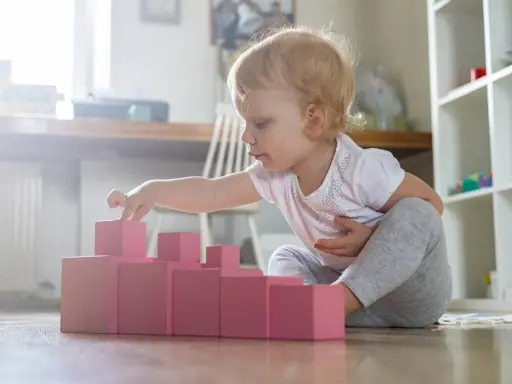 Bambina di 1 anno gioca con blocchi rosa, un'attività divertente in casa per sviluppare la coordinazione.