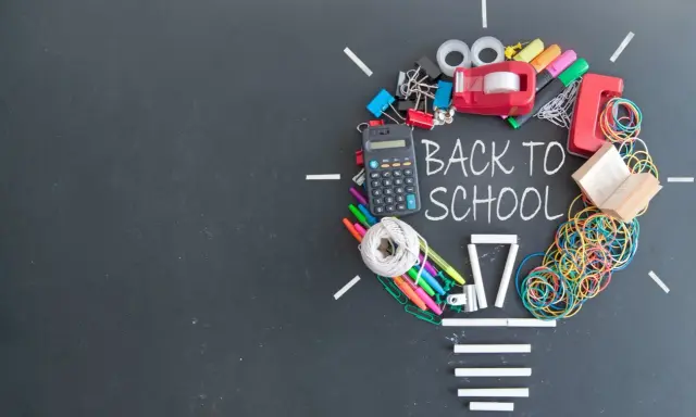Un'idea luminosa per un buon inizio di anno scolastico: calcolatrice, penne, elastici e altri materiali scolastici formano una lampadina su lavagna.