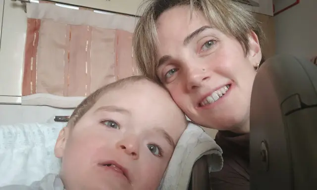 Un bambino con sindrome di down lieve e sua madre sorridono. La sua espressione dolce e i suoi occhi chiari sono un segno di amore.