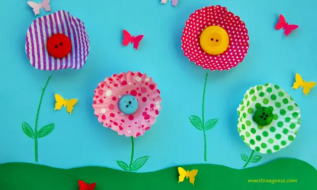 Lavoretti primavera: fiori colorati con bottoni e farfalle di carta su sfondo azzurro.