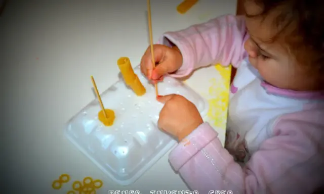 Bambina di 3 anni si diverte con giochi creativi: infila pasta su stecchini, sviluppando manualità e fantasia.