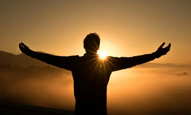 Silhouette di una persona con le braccia aperte al tramonto, immersa nella nebbia dorata. Un momento di pace e buonanotte con gratitudine.