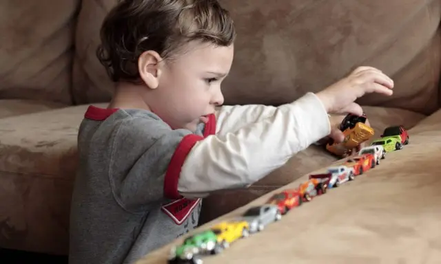 Bambino gioca con macchinine, creando una fila colorata. Le sue mani si muovono con un ritmo ipnotico, un esempio di stimming mani.