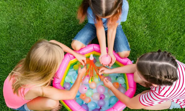 Bambini di 6 anni si divertono con giochi d'acqua in giardino, perfetti per un compleanno estivo.