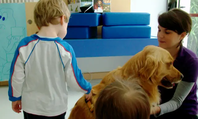 Un bambino interagisce con un cane durante una sessione di pet therapy. La donna sorride mentre il cane è accarezzato.