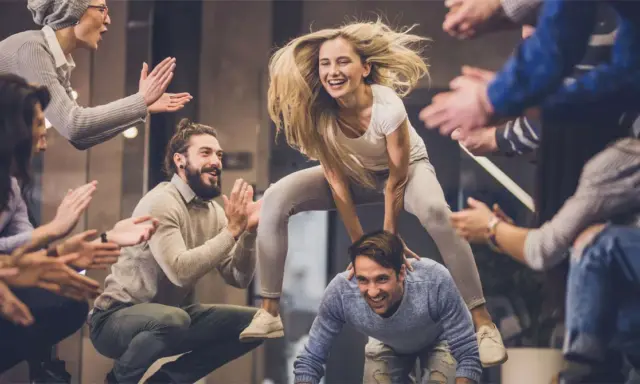 Un gruppo di amici si diverte con giochi da fare in gruppo seduti senza niente, una donna salta su un uomo mentre gli altri applaudono.