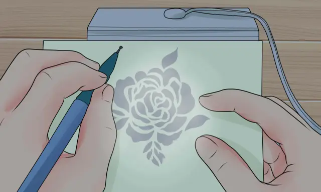 Mani che creano un disegno floreale con uno strumento su carta illuminata, un'arte di embossing su carta.