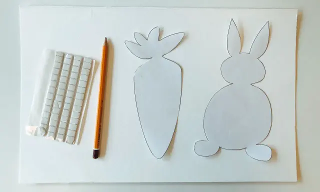 Sagoma di coniglietto e carota, matita e adesivi per creare decorazioni pasquali.