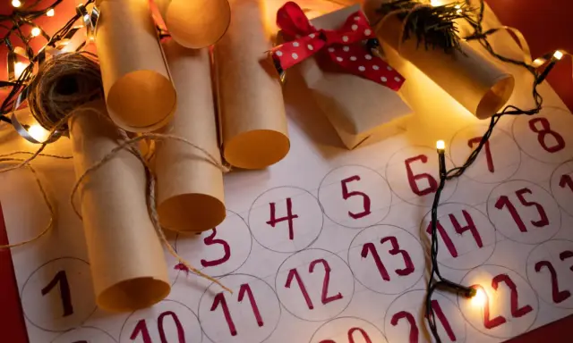 Un **calendario avvento fai da te cartoncino** con rotoli di carta marrone legati con spago, luci natalizie e un piccolo pacchetto regalo.