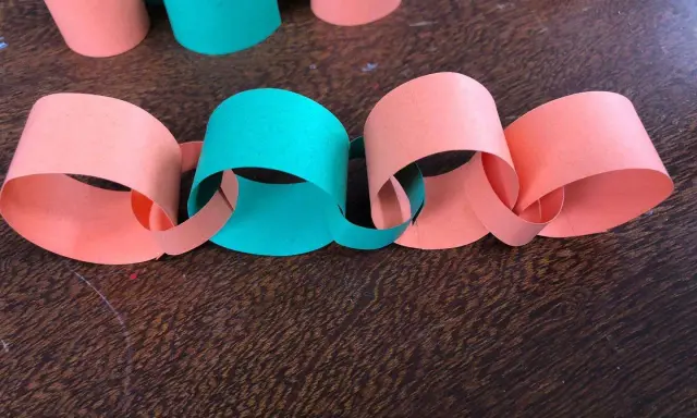 Una catena di carta colorata, con anelli arancioni e verdi intrecciati, pronta per decorare.